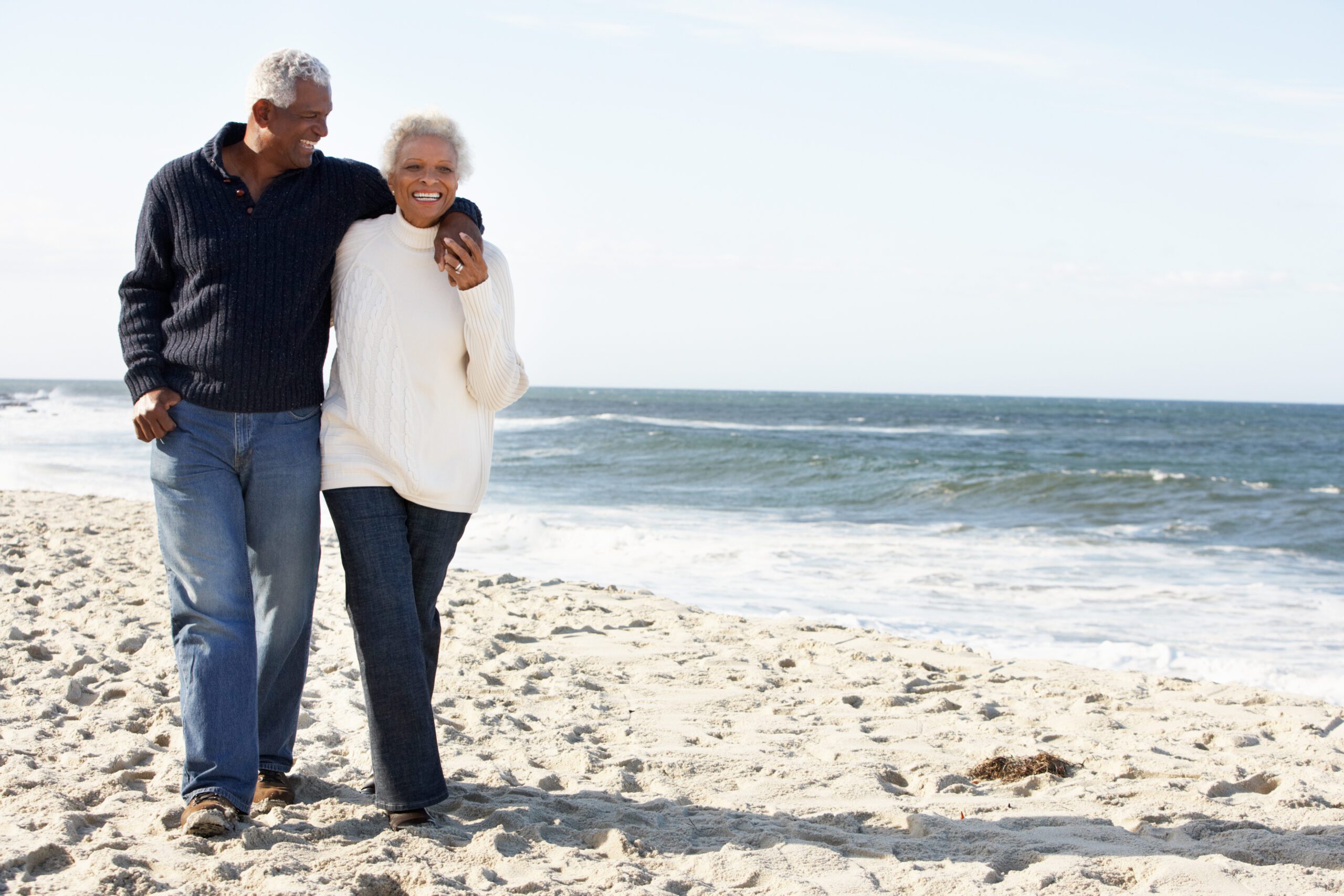 elderly African American couple walking on a white sandy beach