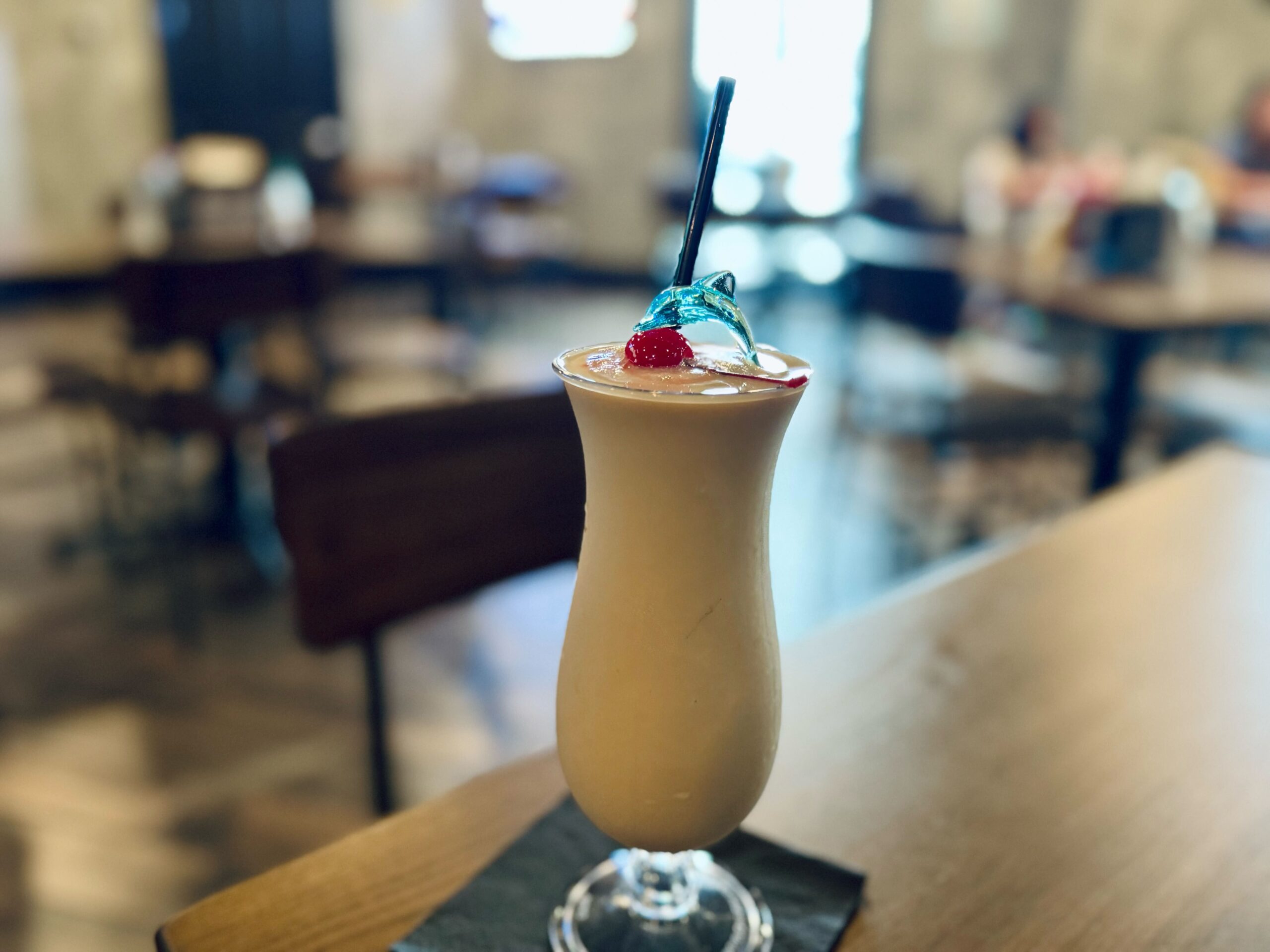 Creamy frozen Bushwacker cocktail garnished with whipped cream, a cherry, and a small umbrella, sitting on a wooden table.